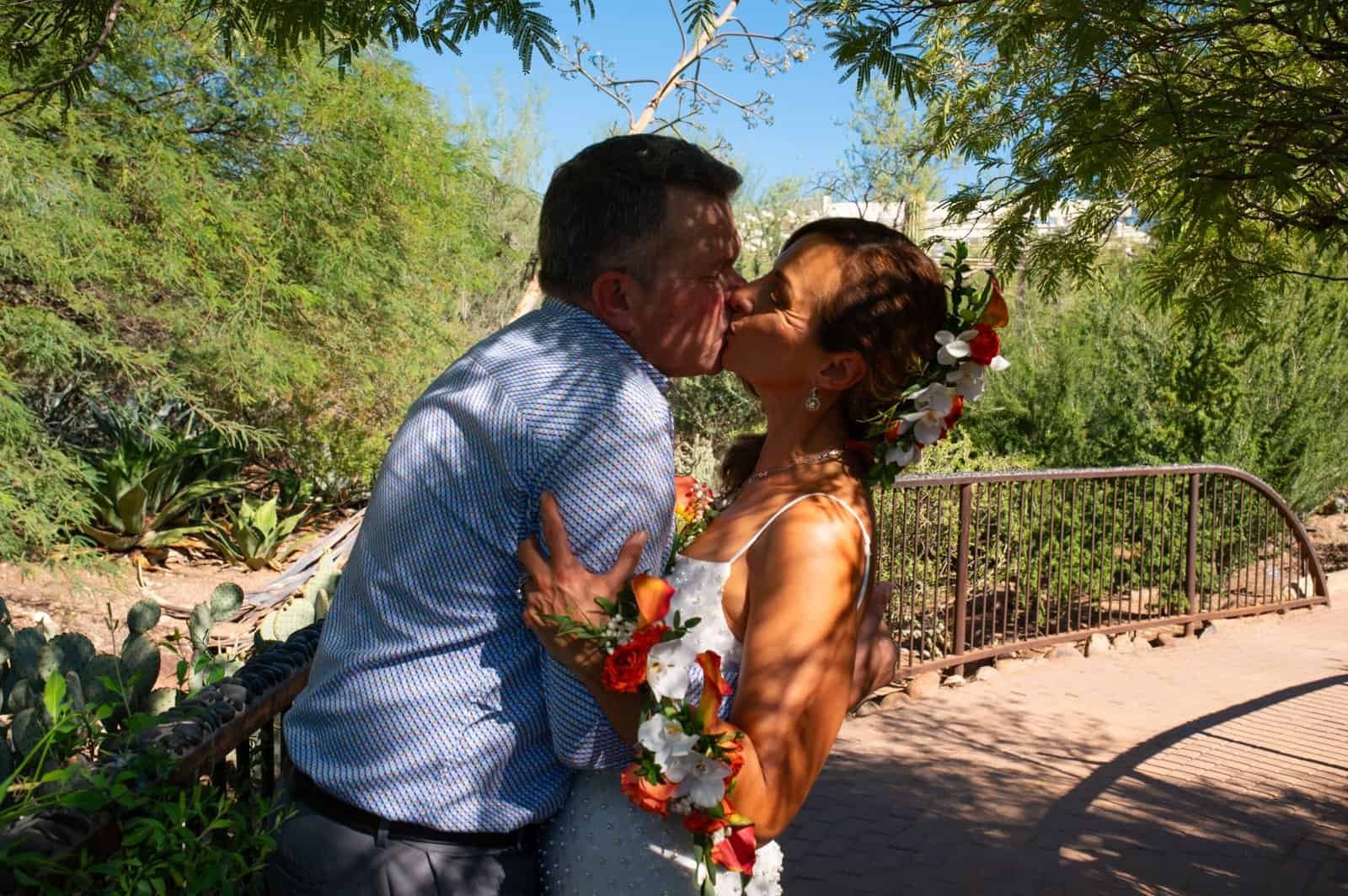 A loving couple shares a tender kiss in a lush, sunny outdoor setting, celebrating their special moment together.