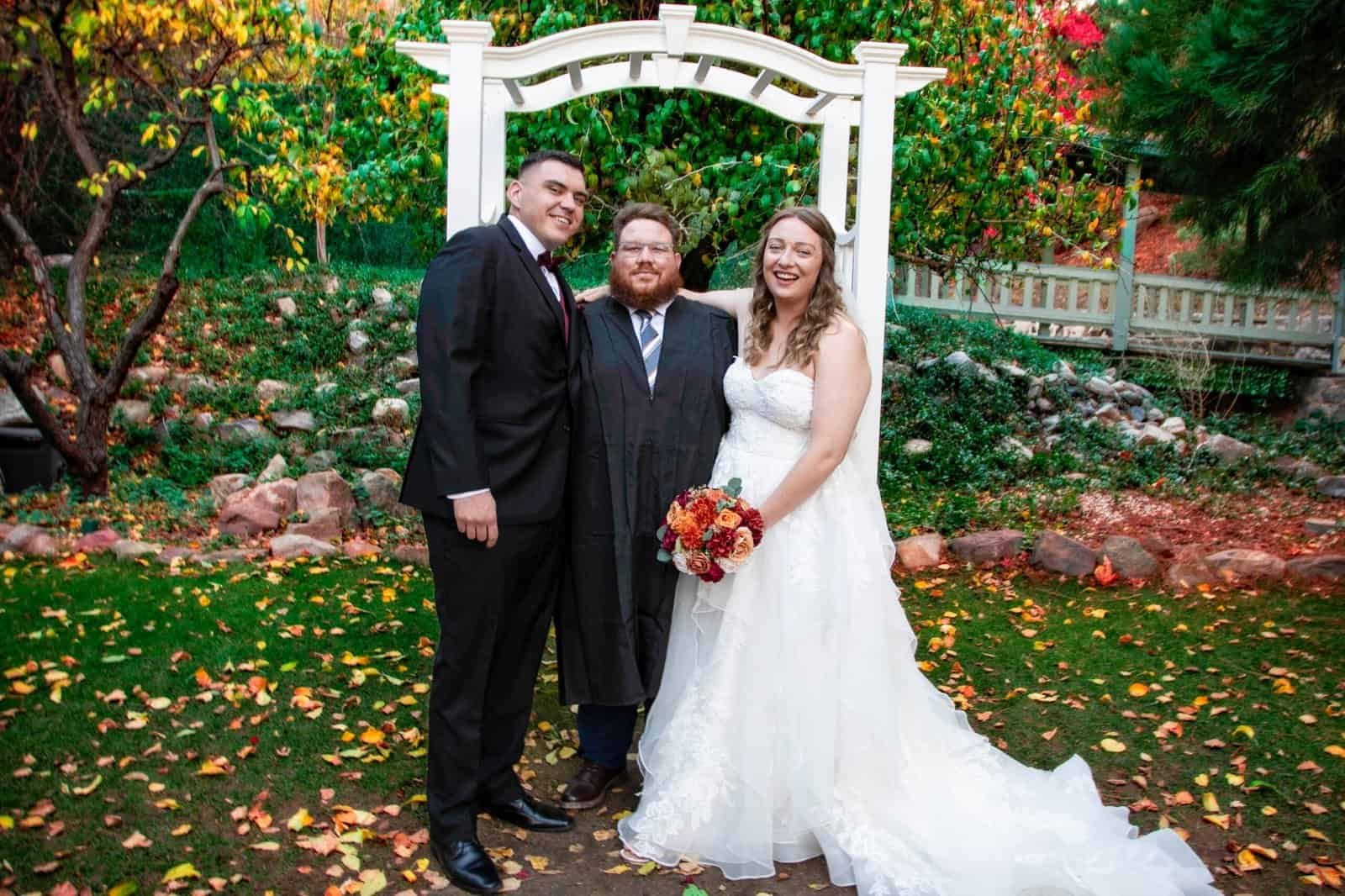Happy wedding moment featuring the bride, groom, and officiant outdoors in a lush garden.