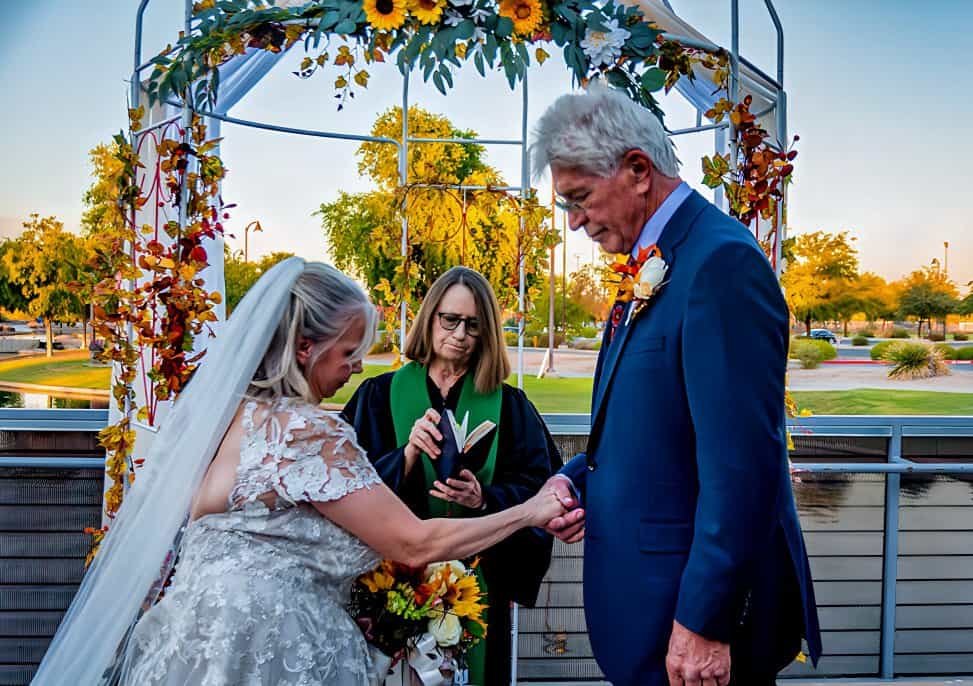 A heartfelt outdoor wedding moment featuring a bride and groom exchanging vows during sunset, with a floral arch backdrop.