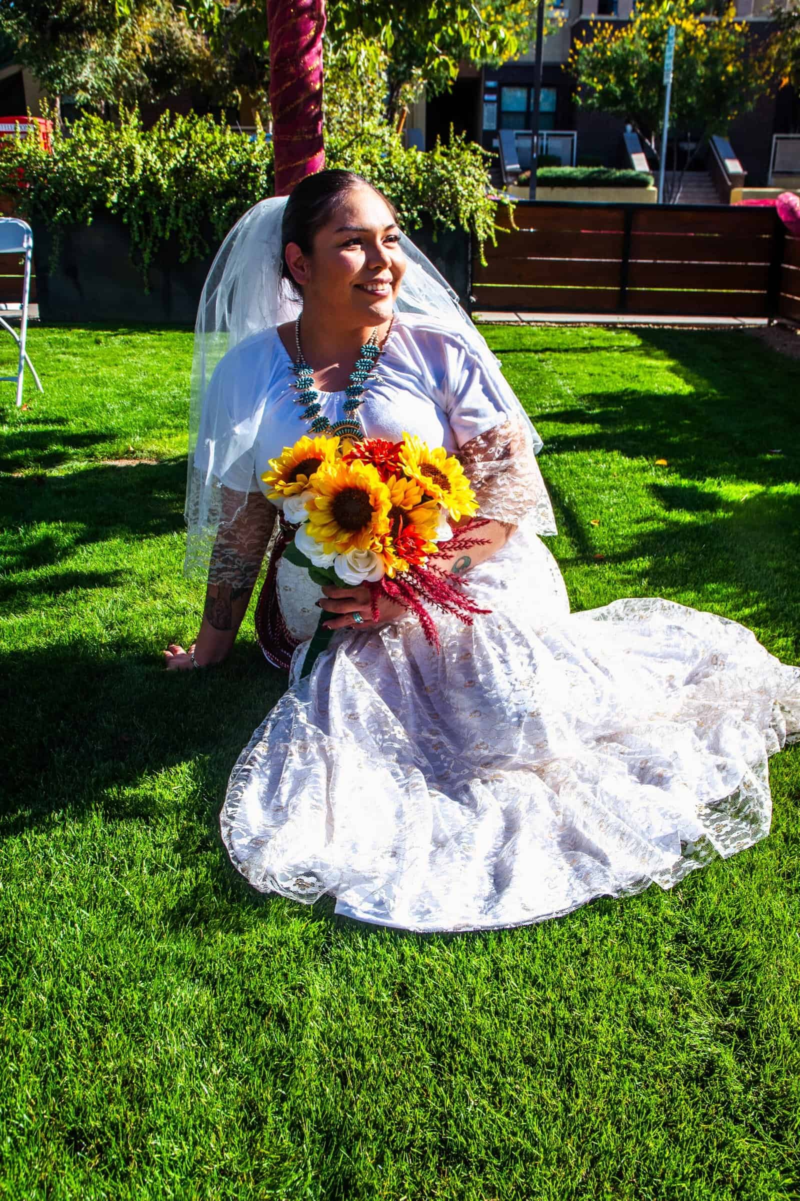 Beautiful bride in wedding dress holding sunflower bouquet, enjoying outdoor garden setting.