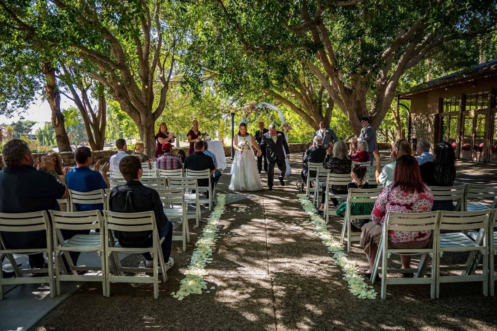 Beautiful outdoor wedding ceremony with guests, bride, and groom in a lush garden setting.