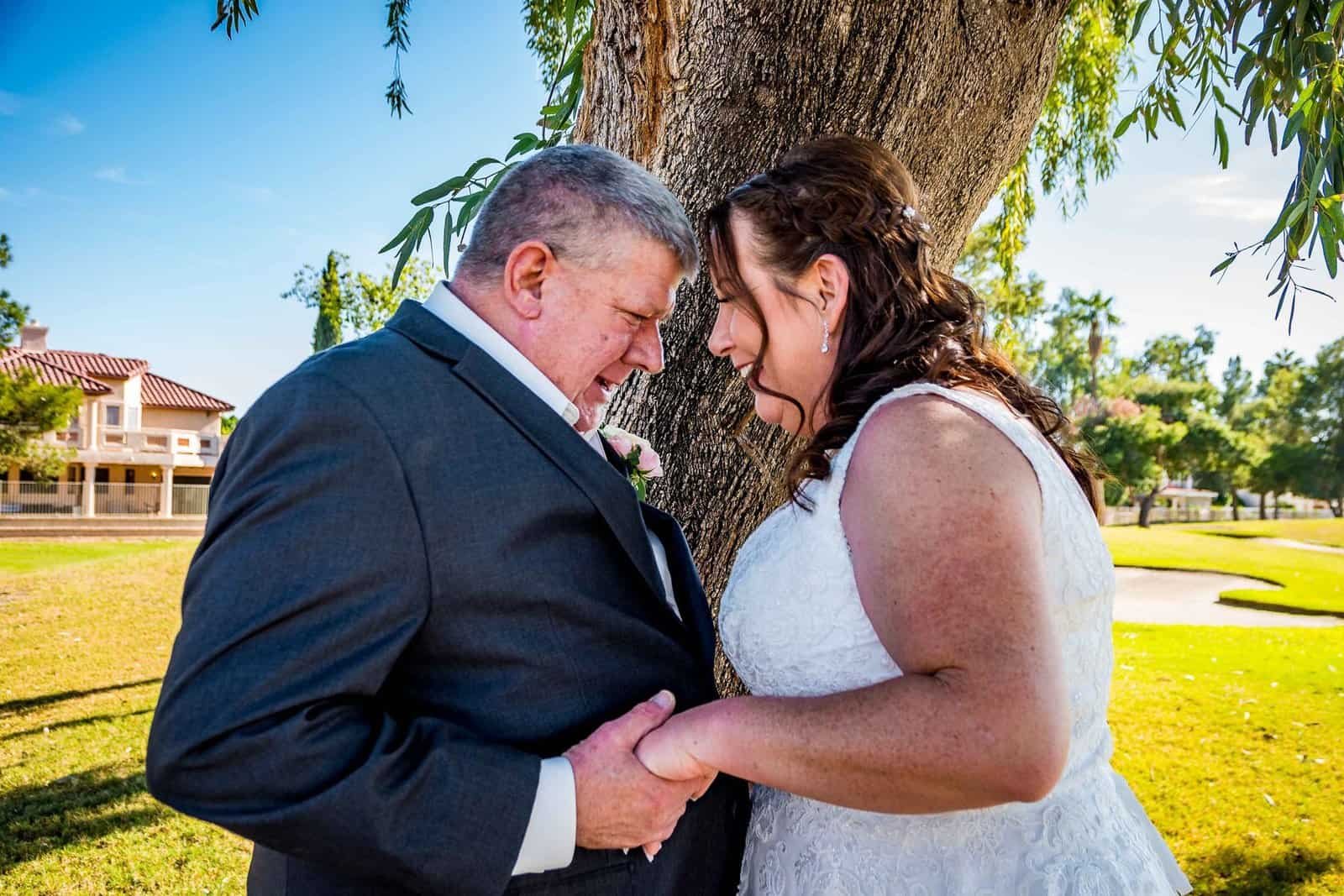 A touching wedding moment captured outdoors with the bride and groom holding hands and sharing a joyful smile.