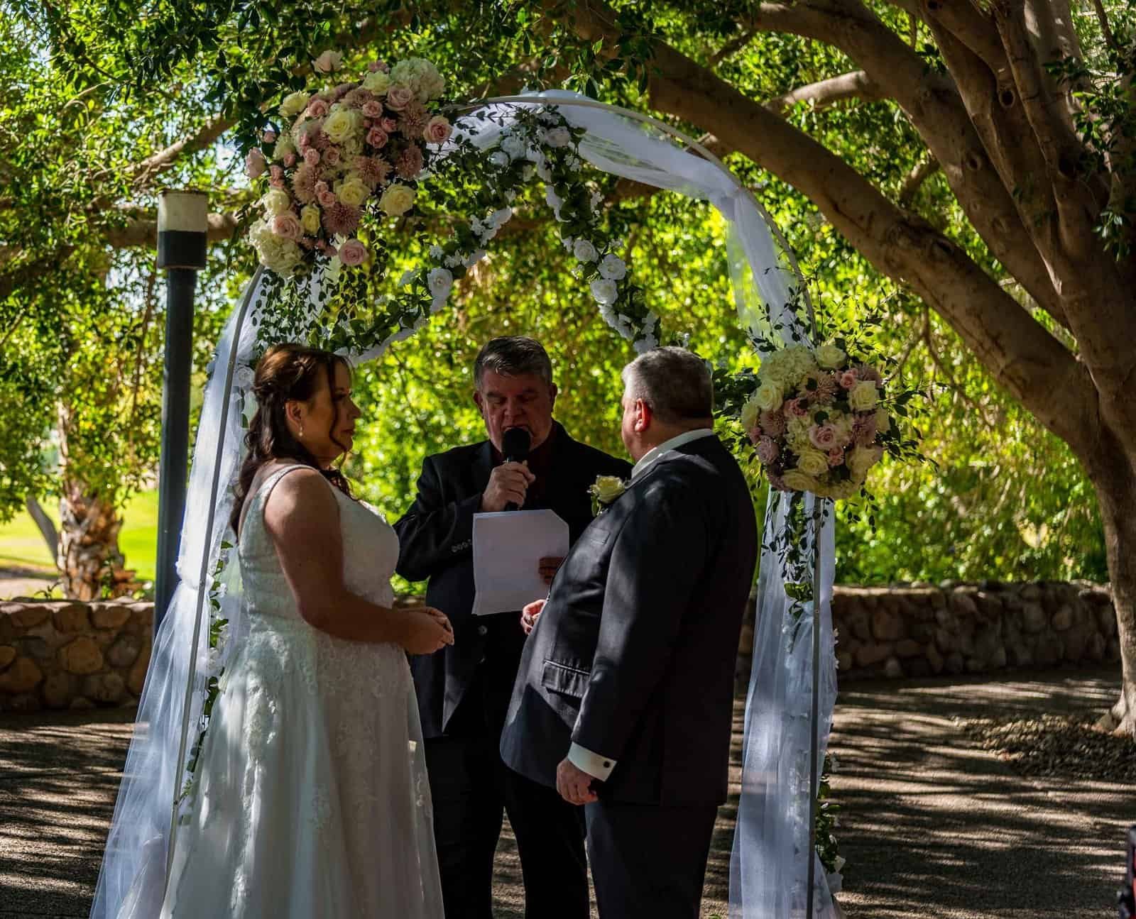 Beautiful outdoor wedding with floral arch, trees, and natural light.