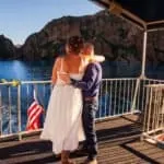 Romantic couple embracing on boat deck with scenic lake and mountains in background.