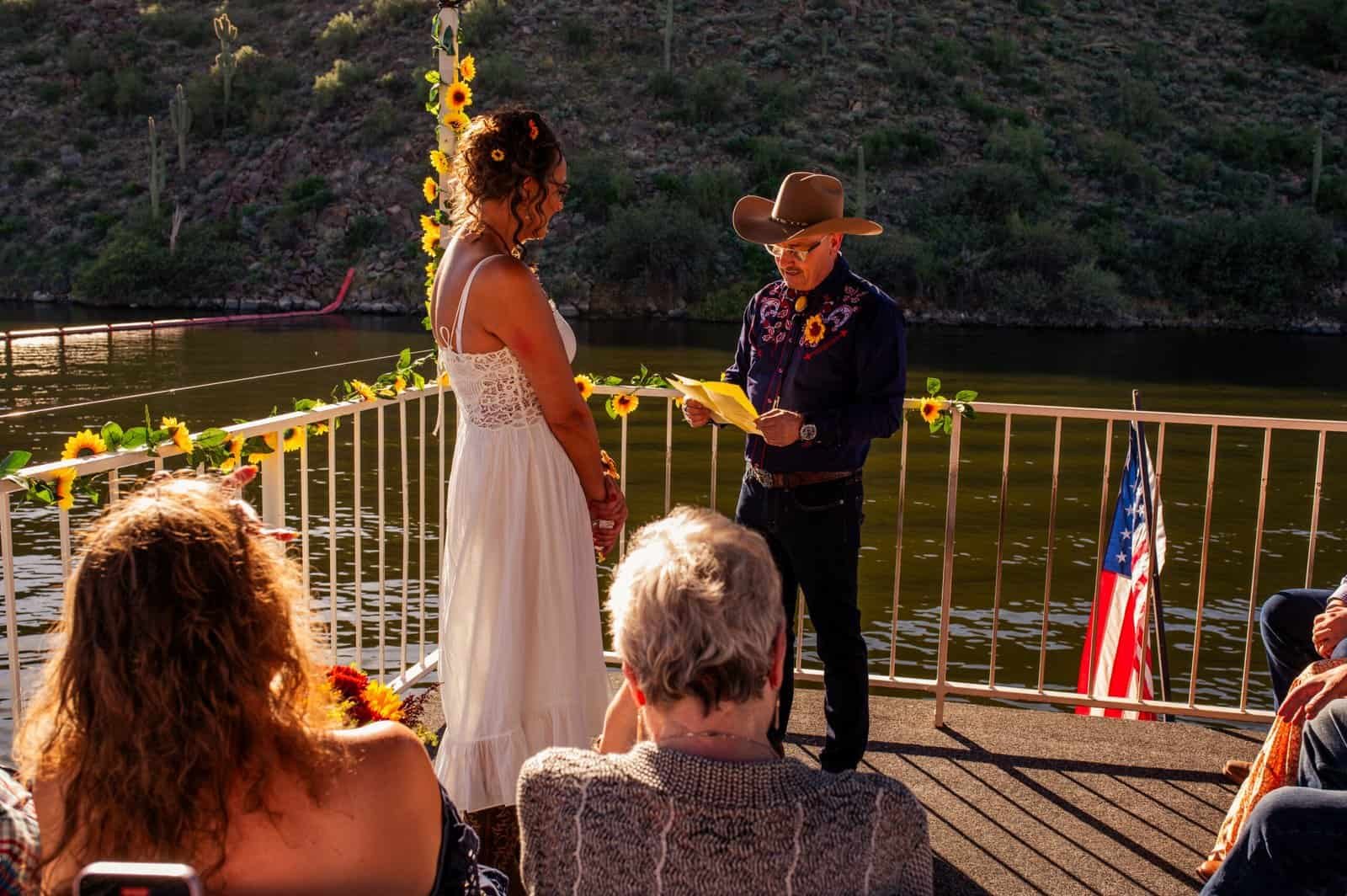 Beautiful outdoor wedding ceremony with the bride and groom exchanging vows on a scenic riverside dock, surrounded by friends and family.