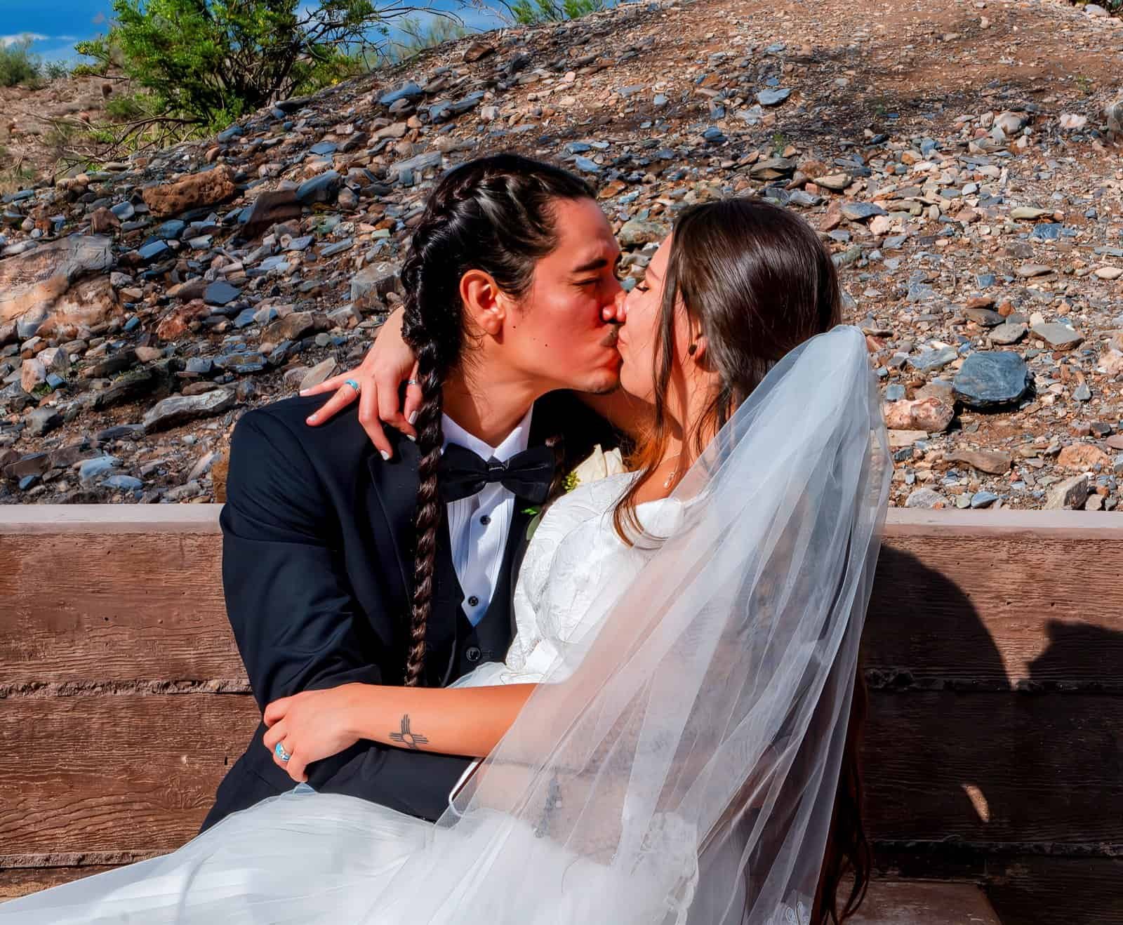 Romantic wedding moment captured with the couple embracing and kissing against a natural rocky background.