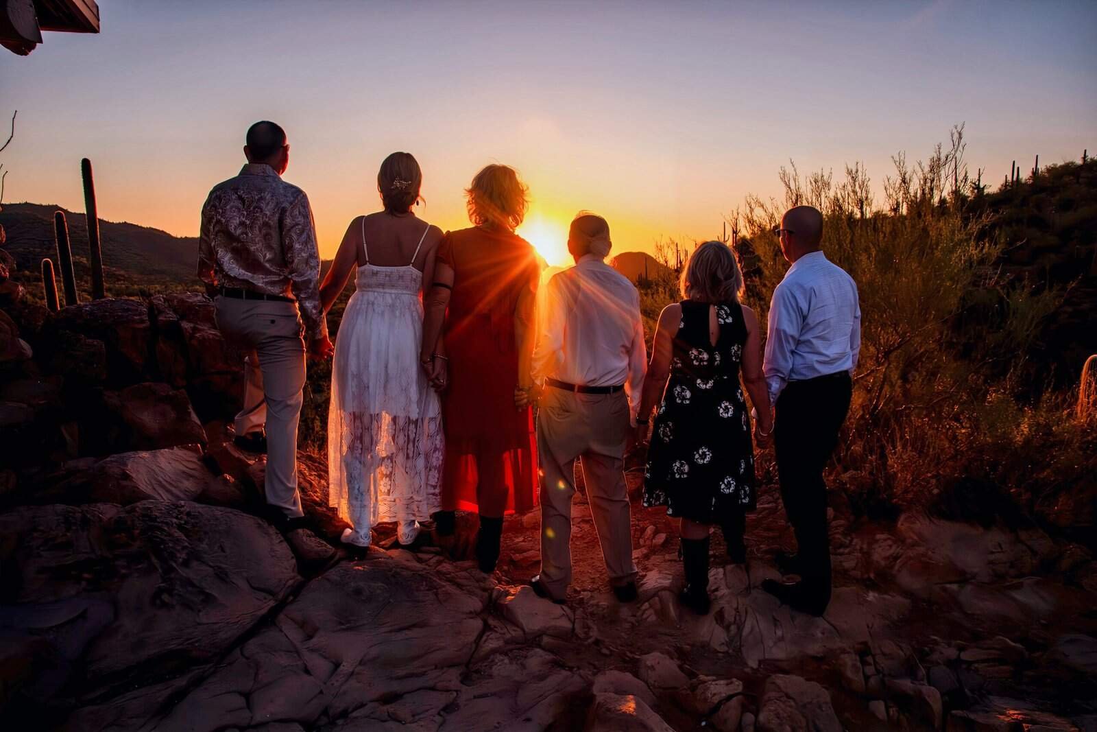 A group of seven family members standing together on rocky terrain, watching a beautiful sunset in a desert setting, capturing a special moment.