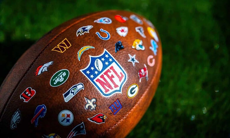 Official NFL football featuring team logos including the New England Patriots, Green Bay Packers, and Kansas City Chiefs on a grassy field.