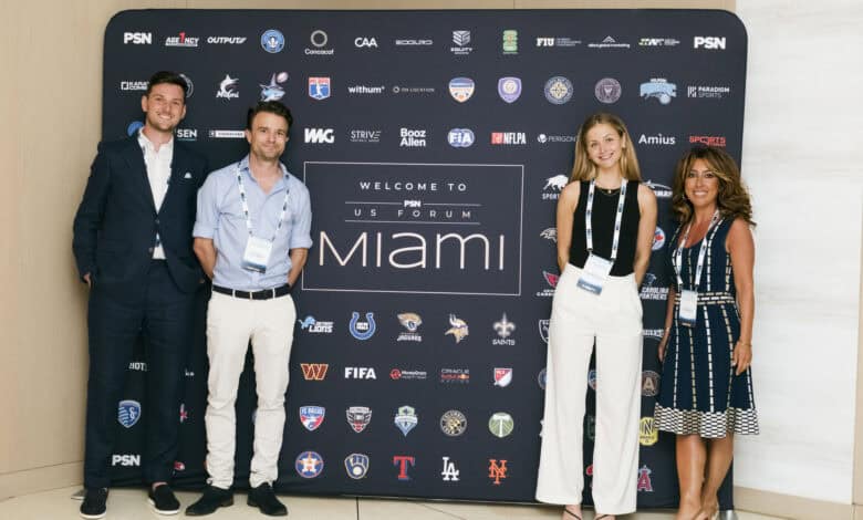 1. Group of professionals attending Sports Insight Miami sports event, standing in front of a branded backdrop with sports logos and team mascots.