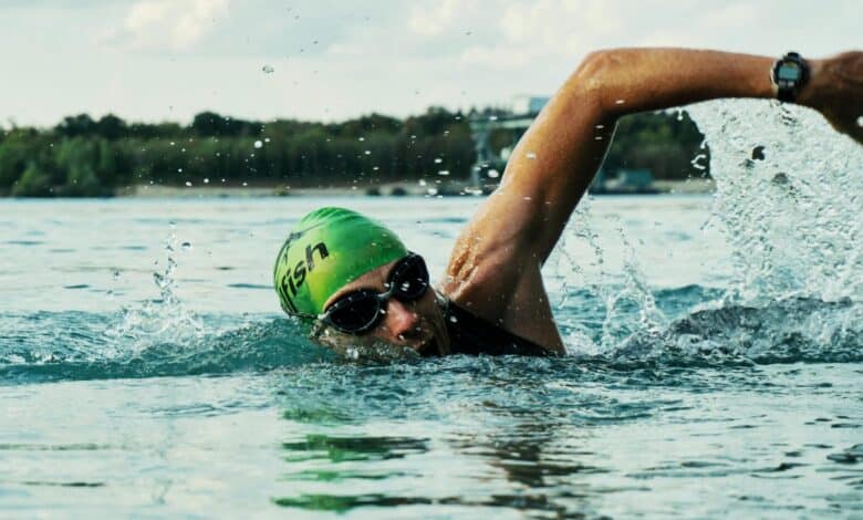 Active swimmer performing open water freestyle swimming in a race, wearing goggles and a green swim cap with 'fish' branding, showcasing competitive sports and training.