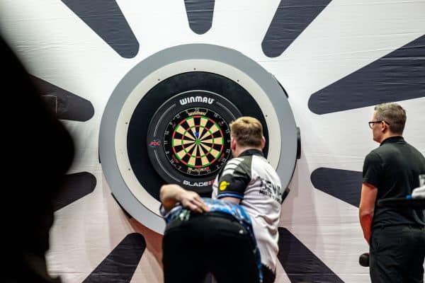Young darts players practicing aiming at a digital target dartboard at a sports event.