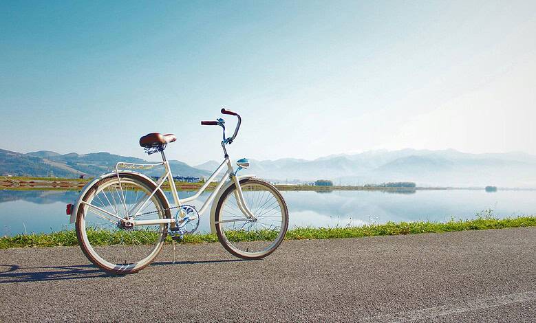 Vintage bicycle parked near a scenic lake with mountains in the background, perfect for outdoor sports and leisure activities.