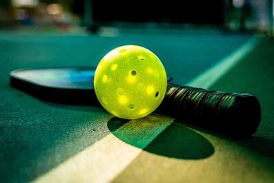 Bright yellow paddleball, tennis racket and ball on indoor table tennis court, ready for match or practice, showcasing sports equipment for table tennis enthusiasts.