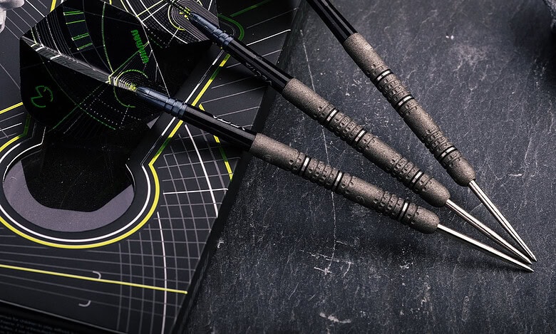 Dart set with black and neon green design on darts, featuring textured grips, placed on a black presentation box, surrounded by rocks on a dark surface. Suitable for sports insight and darts analysis.