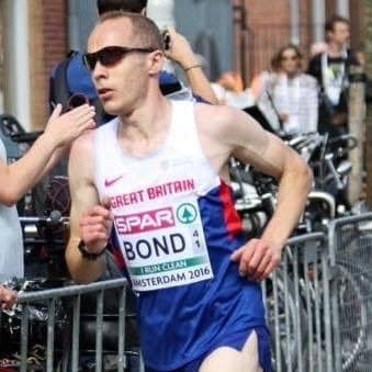 A male athlete wearing sunglasses and a Great Britain running kit participating in a competitive race, surrounded by spectators and event barriers.