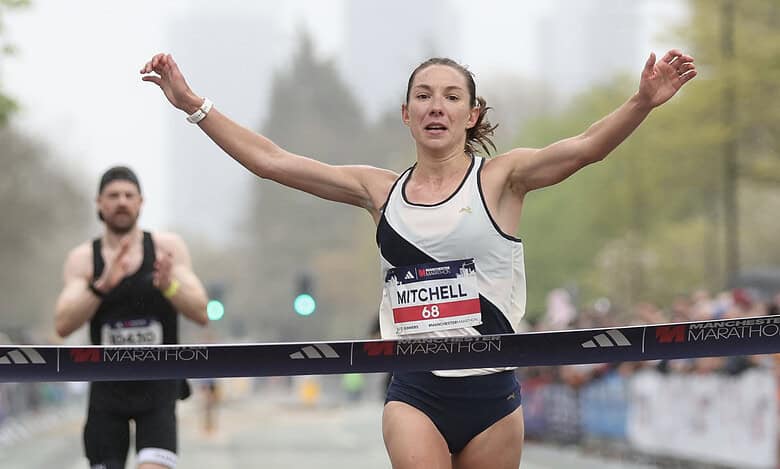Female marathon runner crossing the finish line with arms raised in victory at a marathon event, showcasing athletic achievement and endurance.