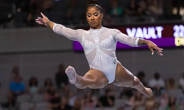 Young female gymnast executing a high jump during a competition, showcasing strength and agility with a focused expression.