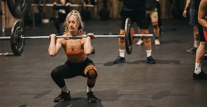 Female athlete performing a squat with a barbell in a gym, demonstrating strength training and fitness.