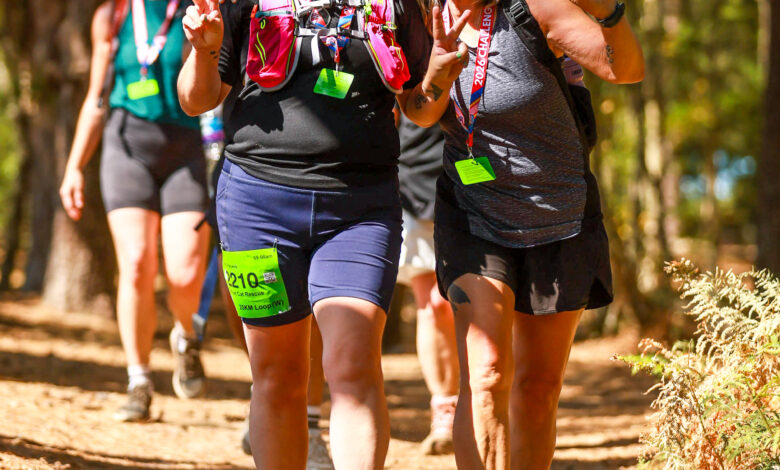 Group of smiling women participating in the Ultra Challenge in Surrey Hills, walking along a forest trail with trees and sunlight.