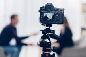 businesswoman in suit giving interview to journalist in office, camera on foreground