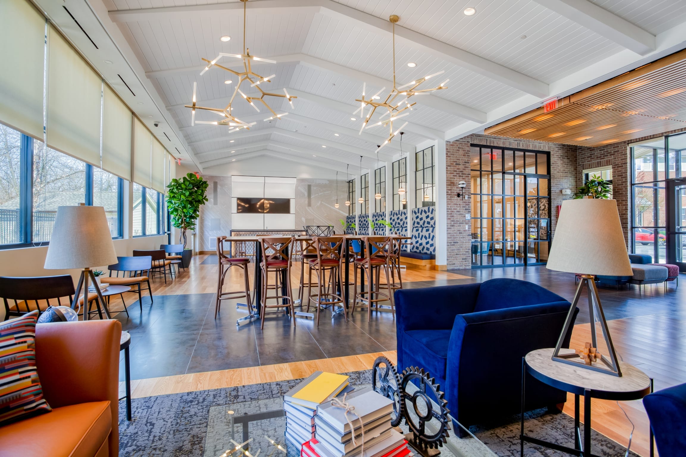 Modern, spacious lounge area at Windsor at Oak Grove with large windows, contemporary light fixtures, comfortable seating, tall tables, potted plants, and decorative accents creates a welcoming and stylish atmosphere.