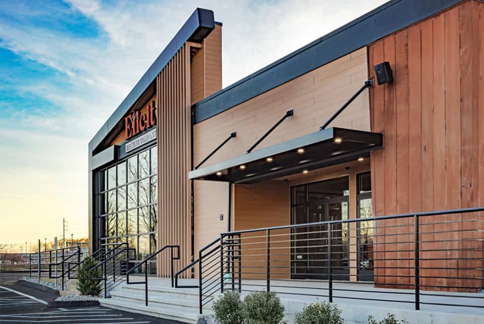 Modern commercial building with wooden and glass facade, featuring a black awning and ramp.