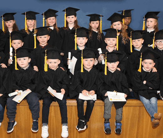 Bright-eyed children in black graduation gowns and caps celebrating a kindergarten graduation ceremony at Thrive Childcare, showcasing early childhood education and achievements.