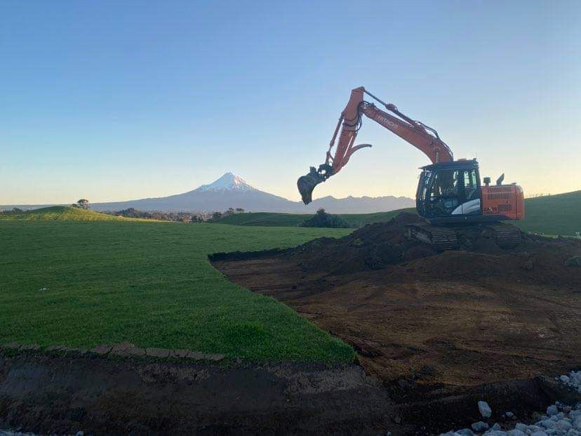 Excavator working on construction site with Mount Taranaki in the background.