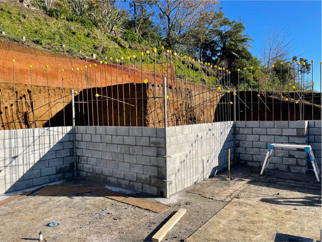 Reinforced concrete retaining wall under construction for slope stabilization and site landscaping, with steel reinforcement bars in place.