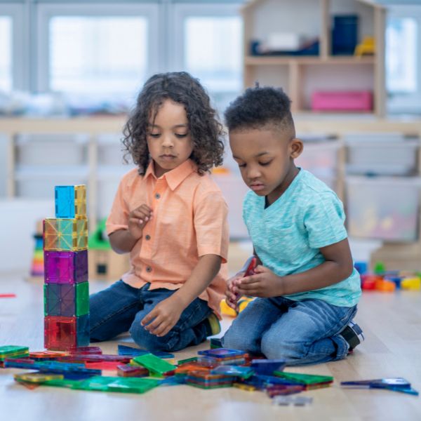 This image shows two young children building a structure with magnetic blocks.