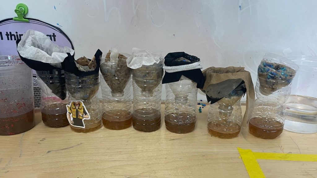This image shows a sample of polluted water, a sample of clean tap water, and 7 DIY water filters created from 20 oz plastic bottles.