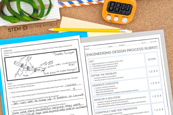 This image shows a student's St. Patrick's Day Snake Removal Tool drawing and prototype. The drawing is on a worksheet. The prototype is created from index cards, wooden craft sticks, and straws. There is also a timer and an engineering design process rubric pictured.