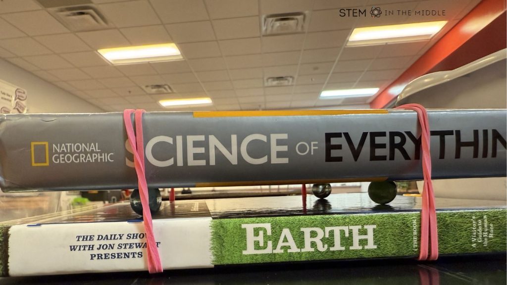 This DIY earthquake table is created by putting marbles between two hardcover books and using rubber bands to secure the books together.