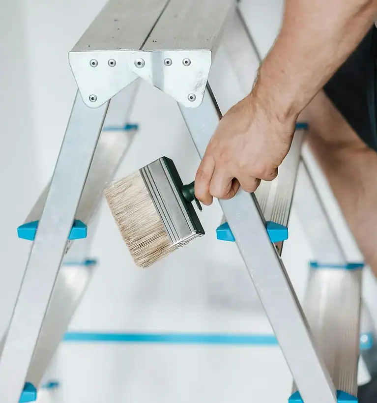 A man is painting a ladder with a brush.