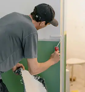 A man is painting a bathroom with a paint brush.