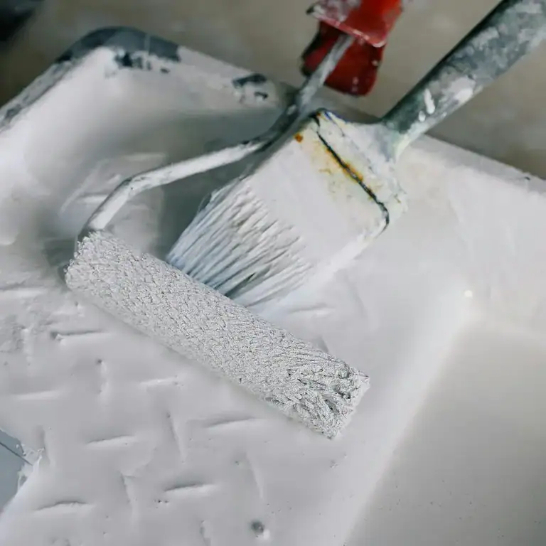 A paint brush and a paint tray with white paint.