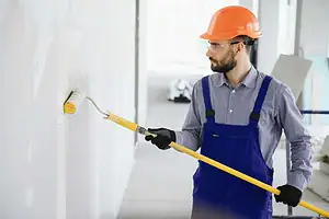 A man in overalls and hard hat painting a wall.