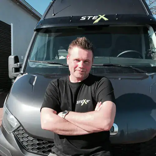 A man in black shirt standing next to a van.