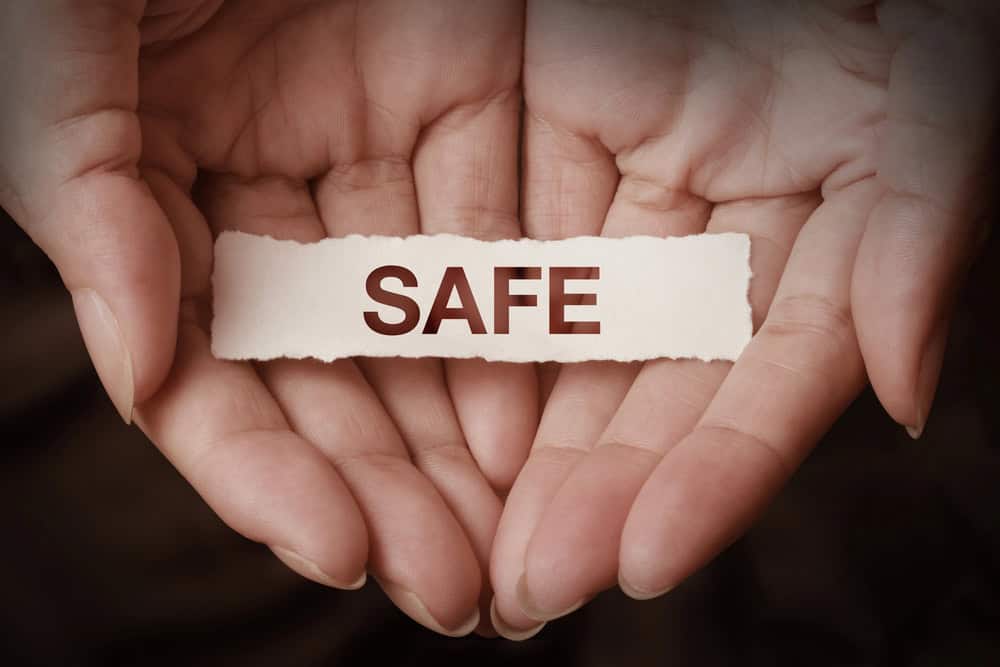 A woman's cupped hands holding a piece of paper with the word SAFE written on it