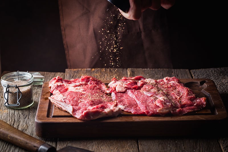 Slicing raw beef steak with seasoning on wooden cutting board for stress and pain relief.