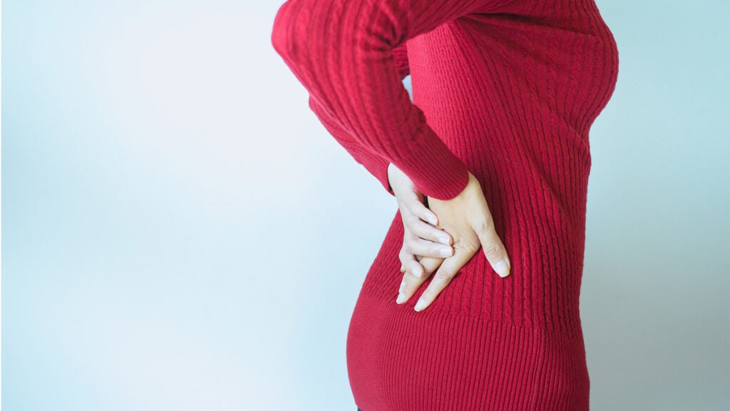 Pain relief for lower back with woman touching her back with her hand.