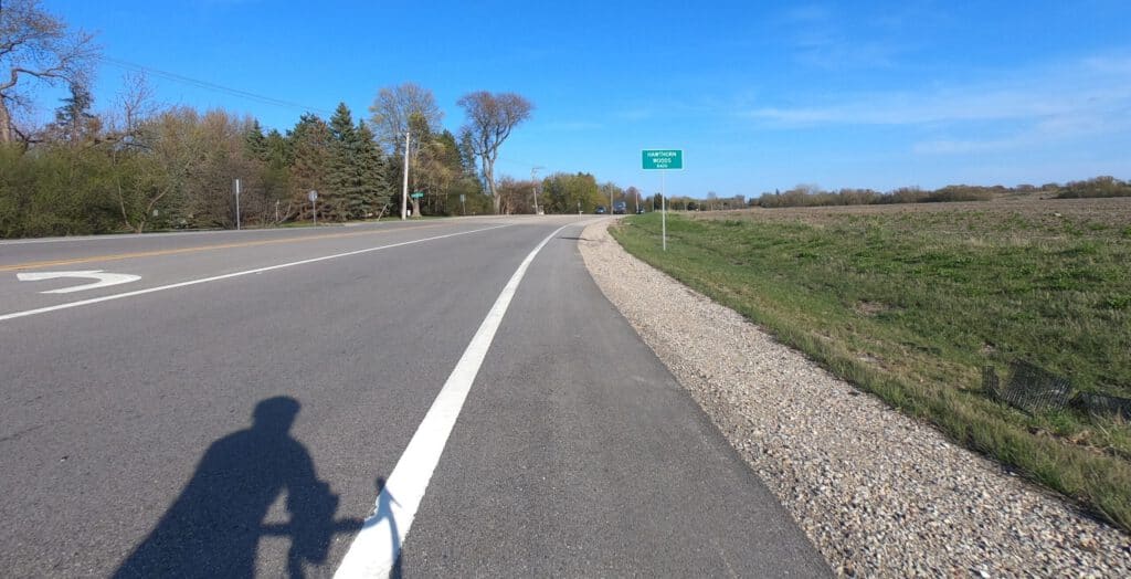 Looking down an asphalt-paved road alongside farmland on a sunny day with a blue sky.
