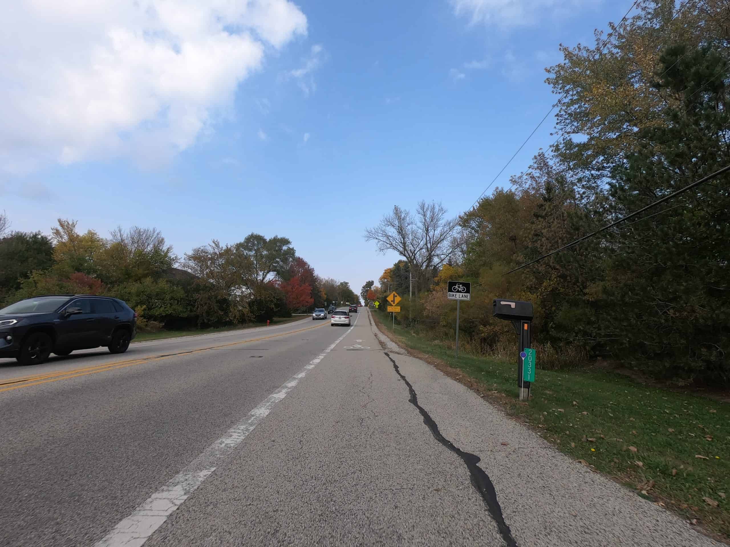 Looking down a colorful tree lined two-lane road with cars in the distance.