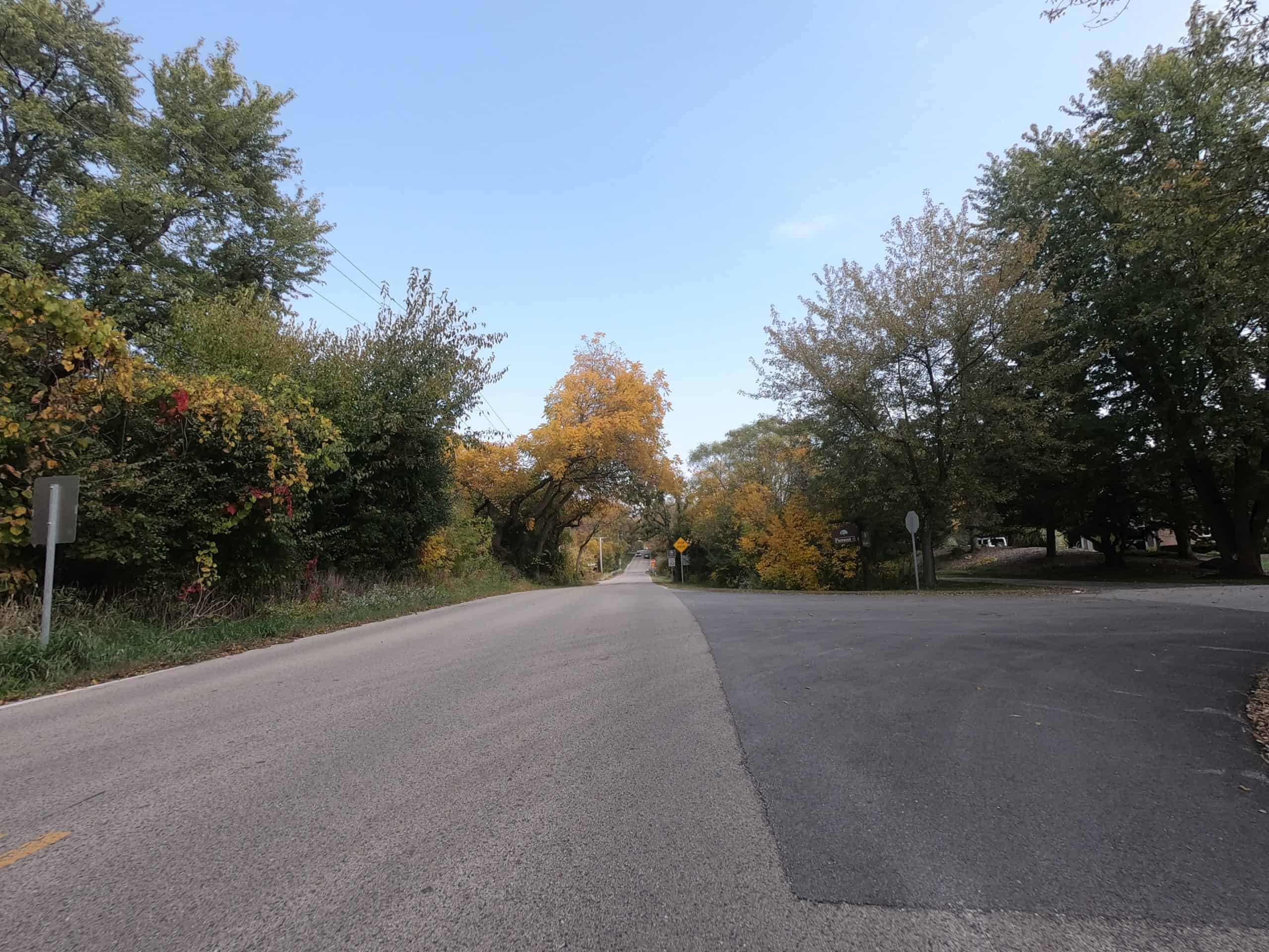 Looking down a colorful tree lined two-lane road.
