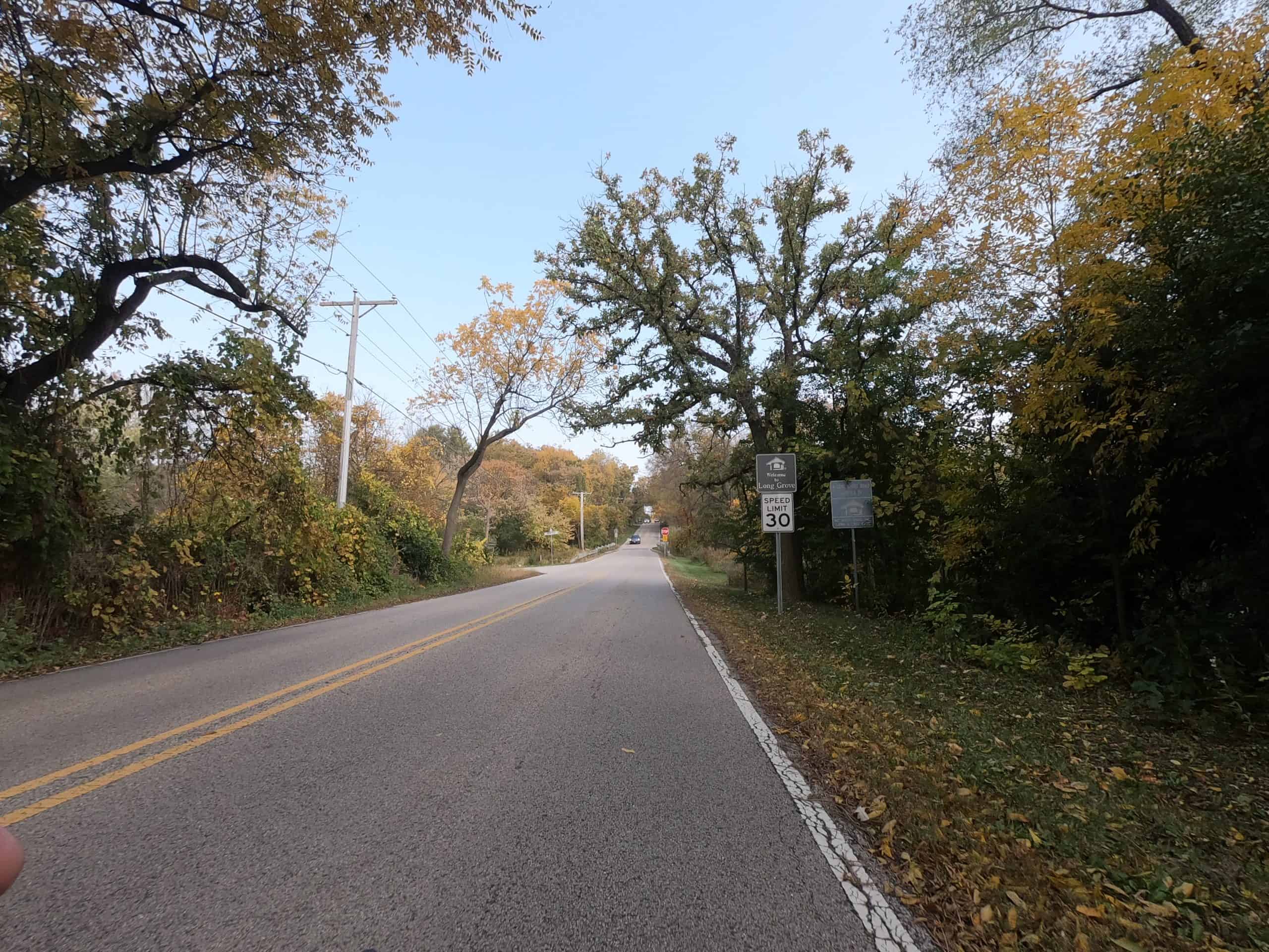Looking down a colorful tree lined two-lane road.
