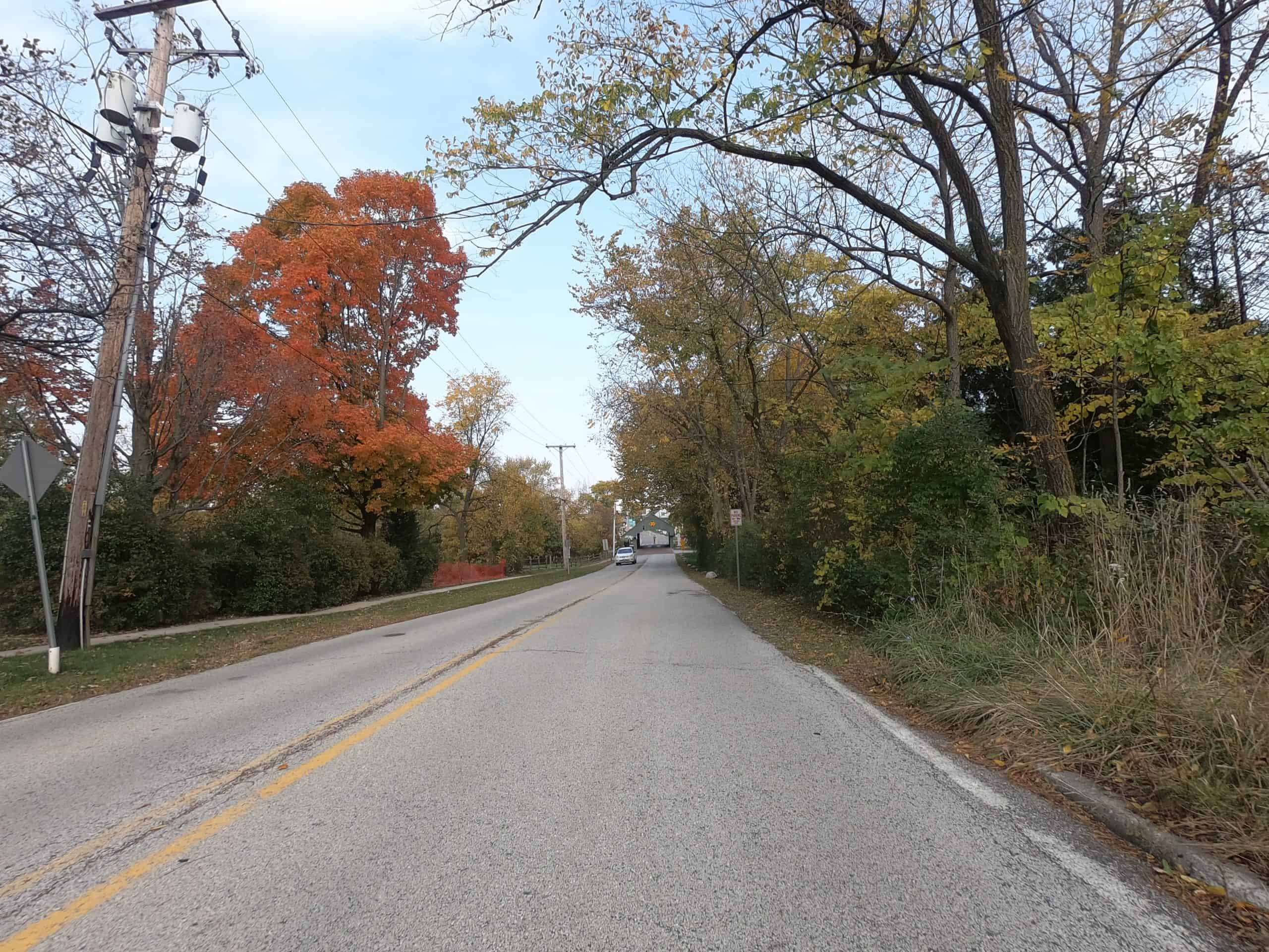 Looking down a colorful tree lined two-lane road.