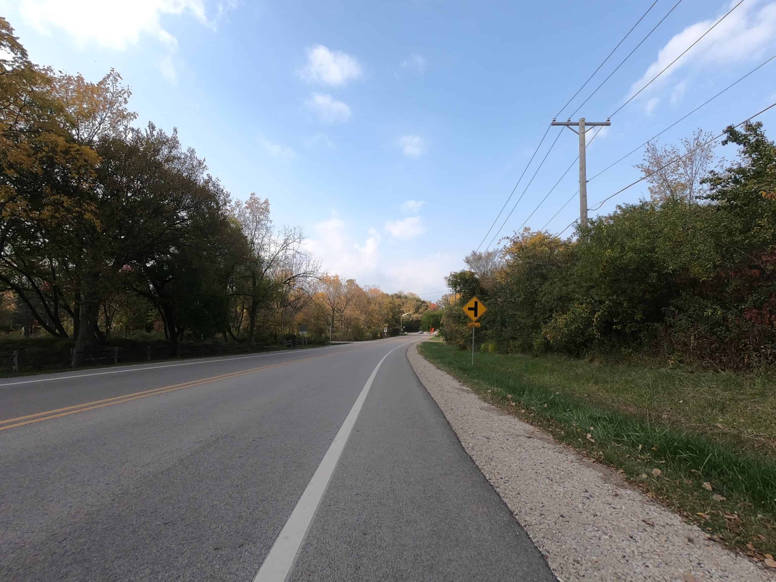 Looking down a colorful tree lined two-lane road.