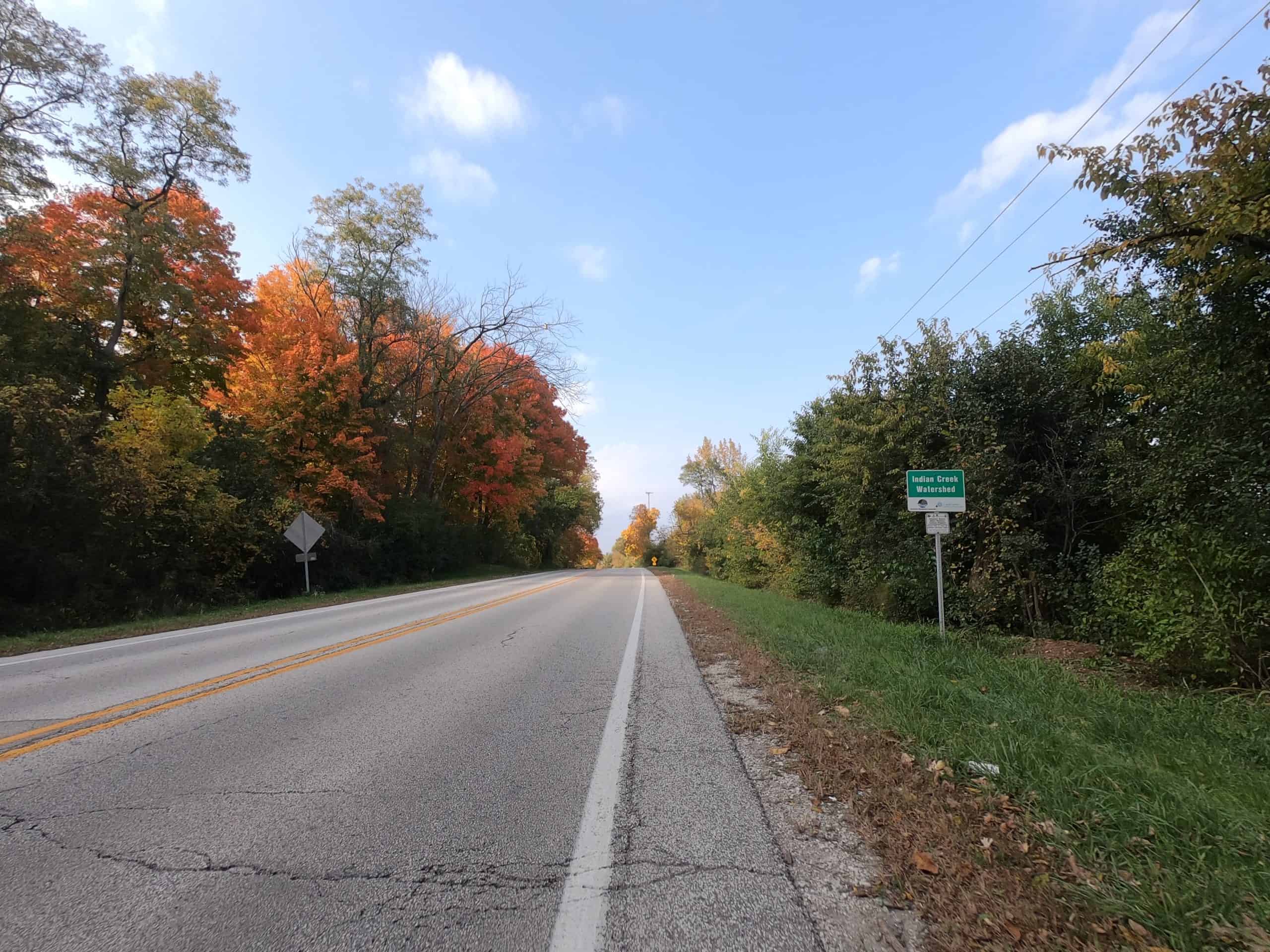 Looking down a colorful tree lined two-lane road.
