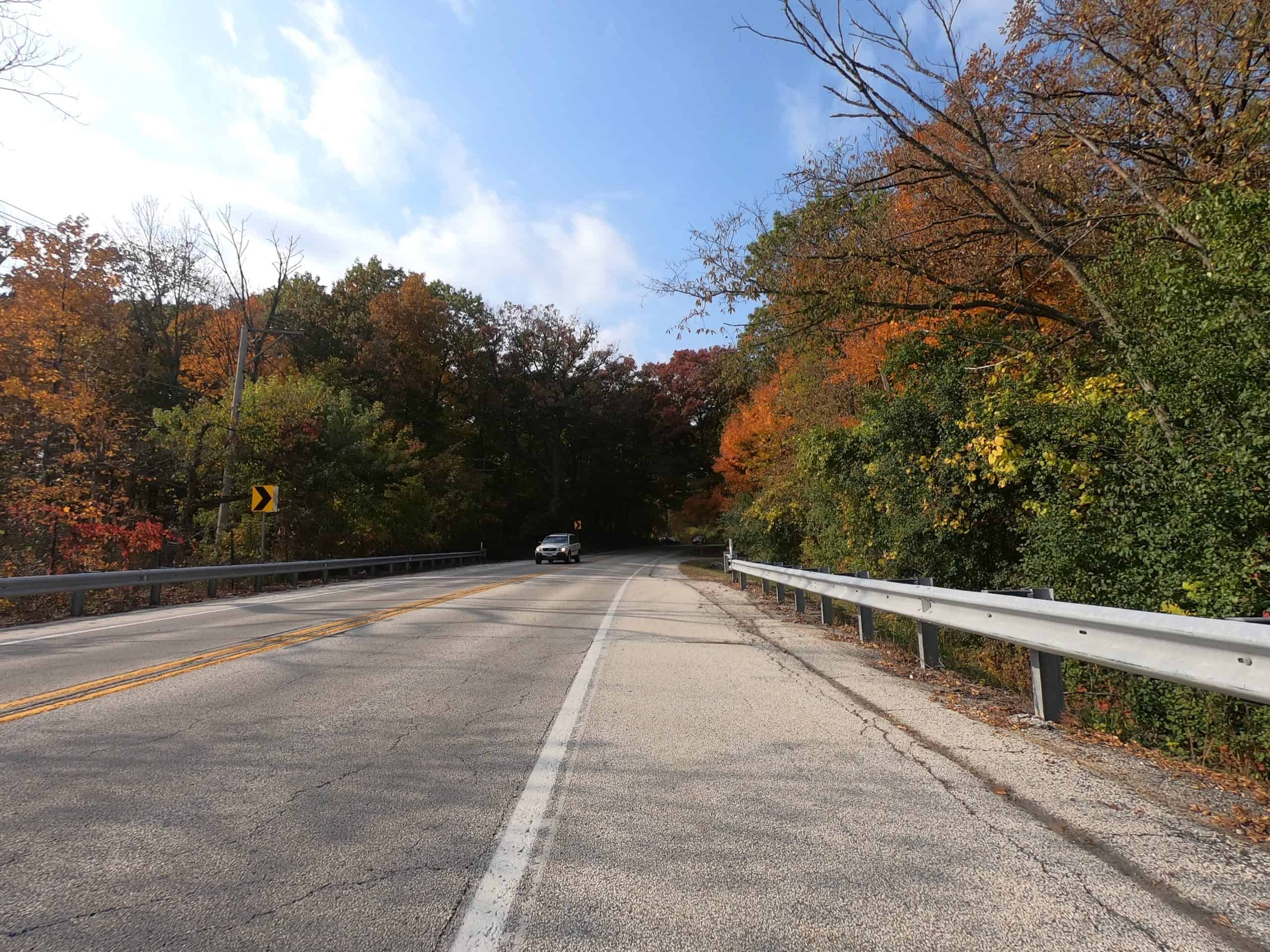 Looking down a colorful tree lined two-lane road.