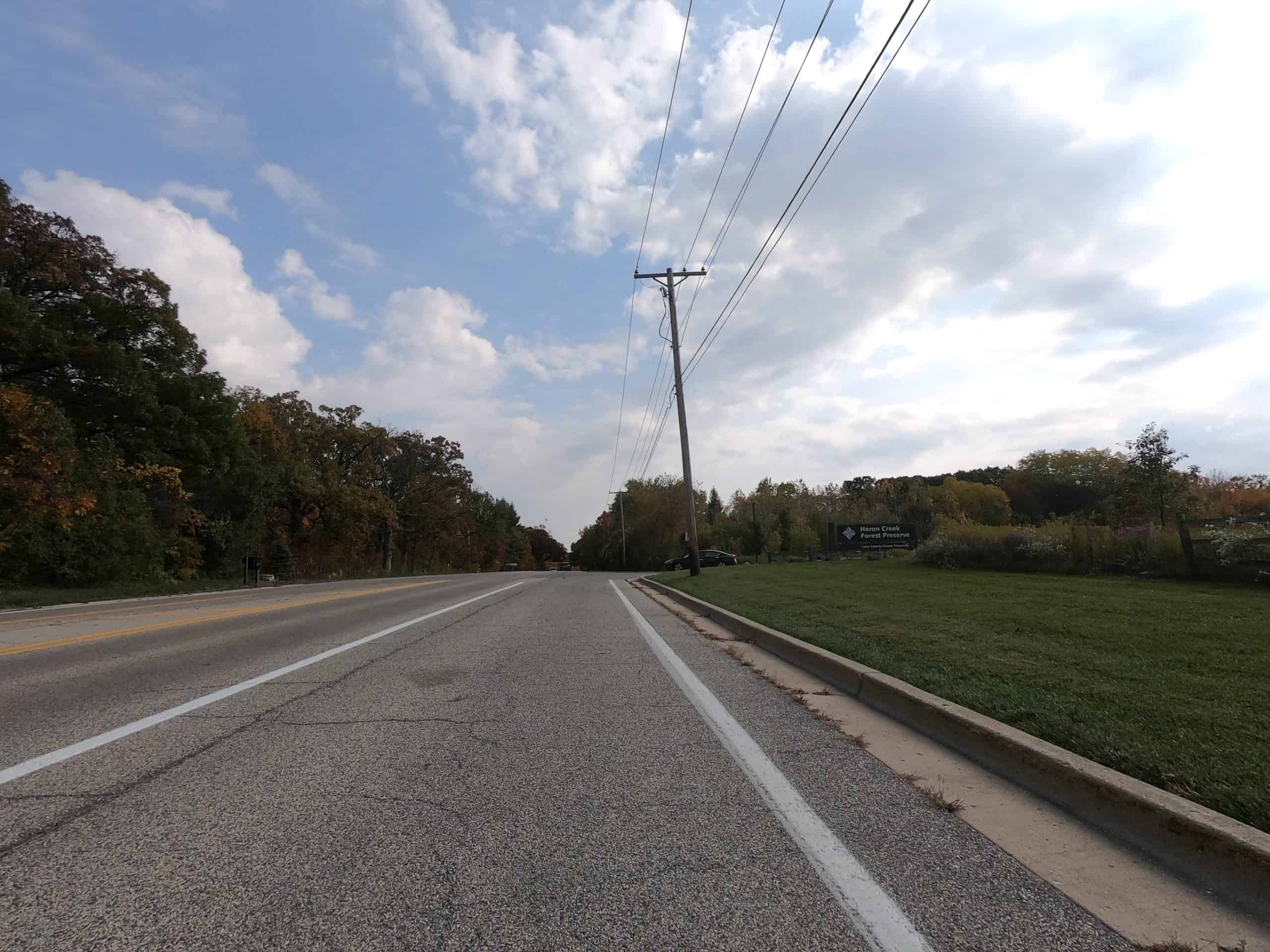 Looking down a colorful tree and meadow lined two-lane road.